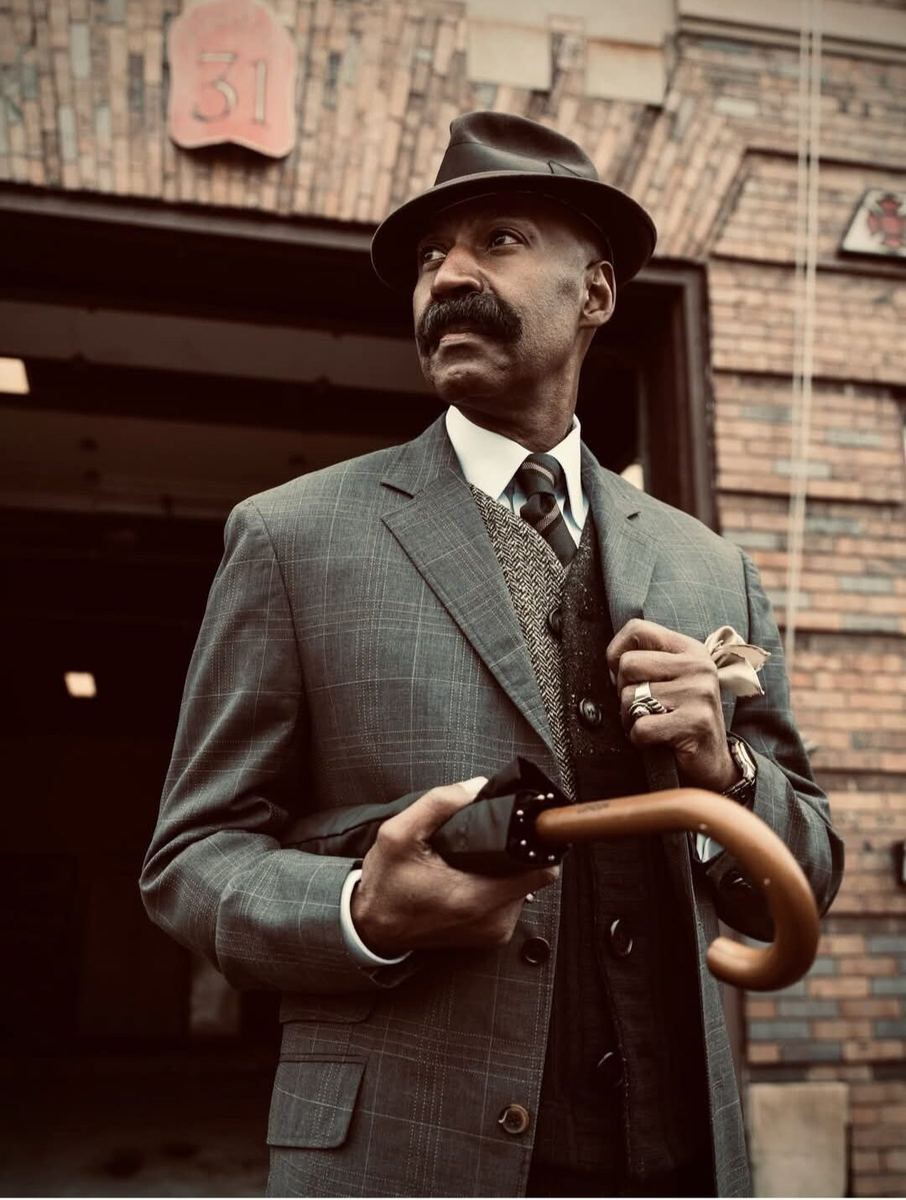 Customer in a brown tweed suit, patterned tie and felt fedora outside the Label Legends storefront